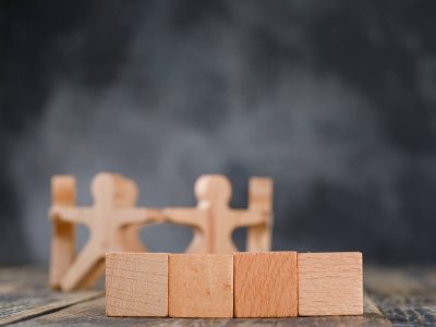 Business success and teamwork concept with wooden figures of people, cubes on wooden and foggy background side view.