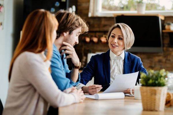 Happy financial advisor and young couple communicating while going through paperwork during a meeting.