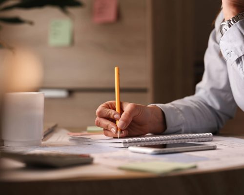 Unrecognizable businesswoman working in the office and writing business plans in her notebook.